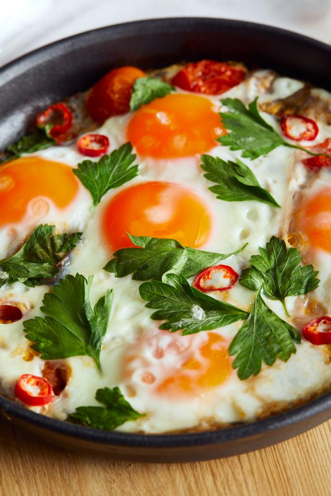 close up view of fried eggs with parsley and chili pepper in pan on wooden table - Photo, Image