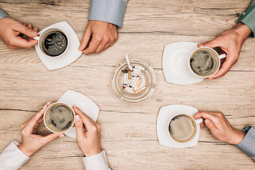 Vista superior de pessoas de negócios bebendo café ao lado de cinzeiro na mesa, vista cortada
 - Foto, Imagem