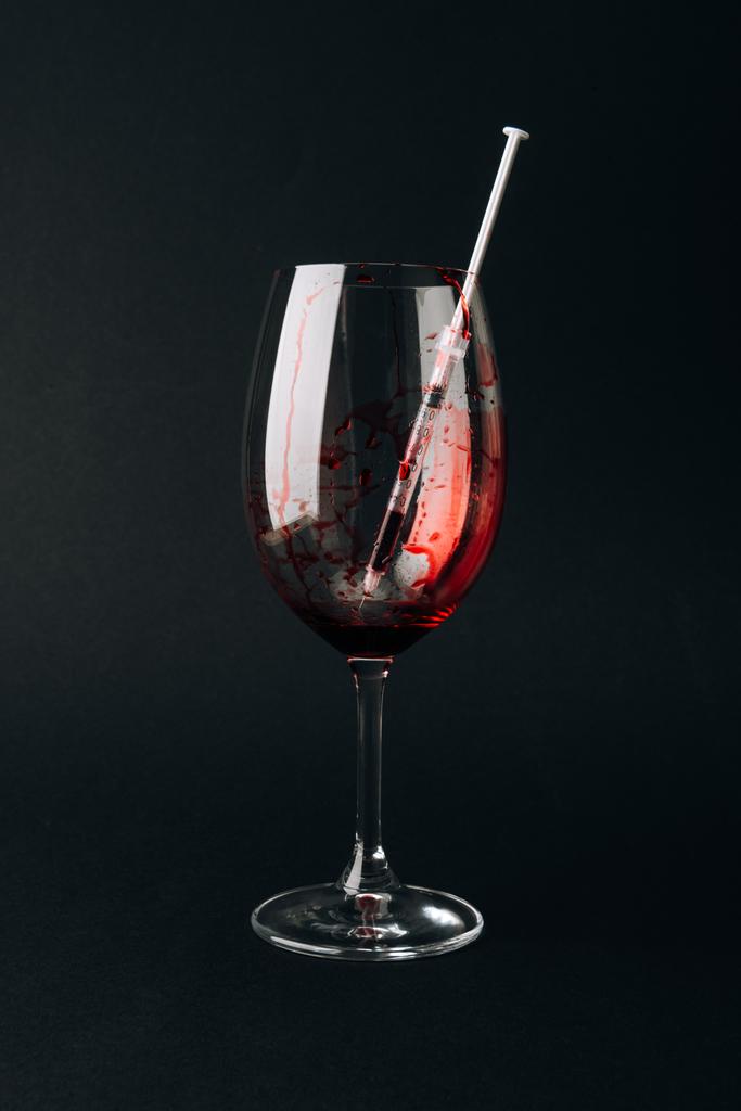 Wine glass with syringe and blood isolated on black - 写真・画像