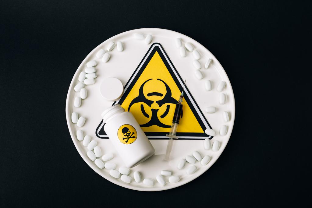 Top näkymä pillereitä, ruisku ja purkki lautasella biovaara merkki eristetty musta
 - Valokuva, kuva