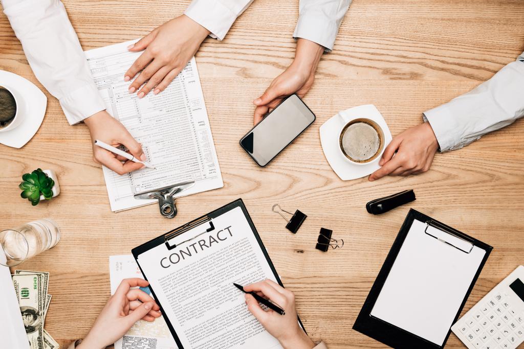 Вид сверху на бизнес-партнеров с договором, бумагой и кофе на деревянном столе
 - Фото, изображение