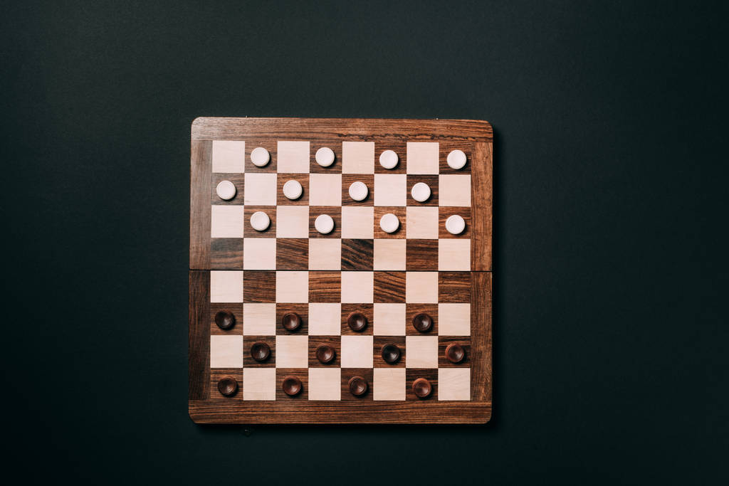 Top view of checkers on wooden checkerboard isolated on black - Photo, Image