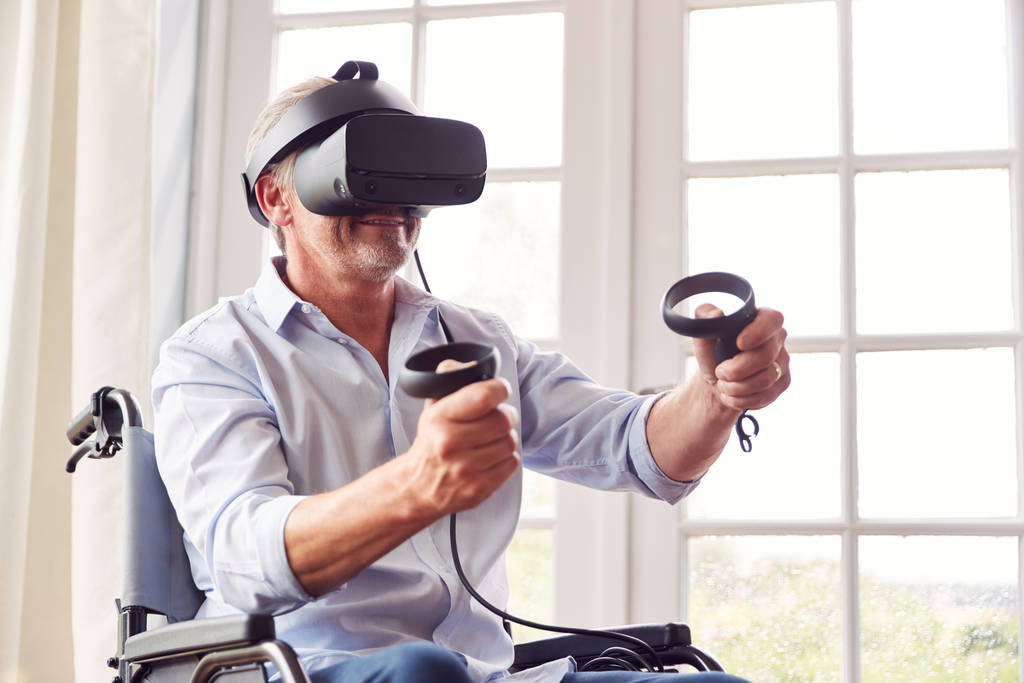 maturo disabile uomo in sedia a rotelle a casa indossando realtà virtuale auricolare Holding controller di gioco
 - Foto, immagini