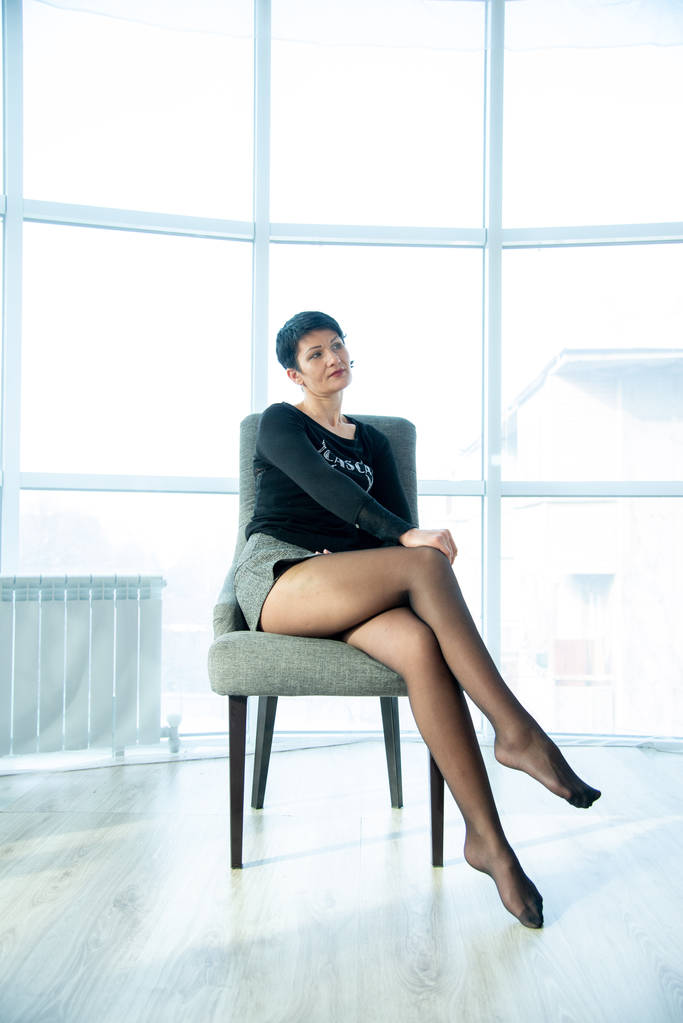 kobieta w czarnym swetrze i szare szorty siedzi na fotelu w studio fotograficznym  - Zdjęcie, obraz