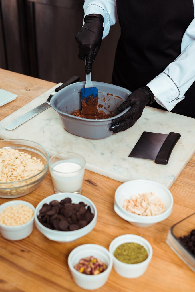 vista recortada del chocolatero sosteniendo espátula de silicona mientras mezcla chocolate en un tazón
  - Foto, imagen
