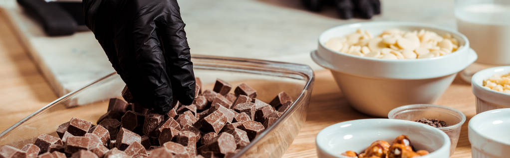 panoramiczny strzał czekoladowy w czarnej rękawicy lateksowej biorąc ciemne kostki czekolady - Zdjęcie, obraz