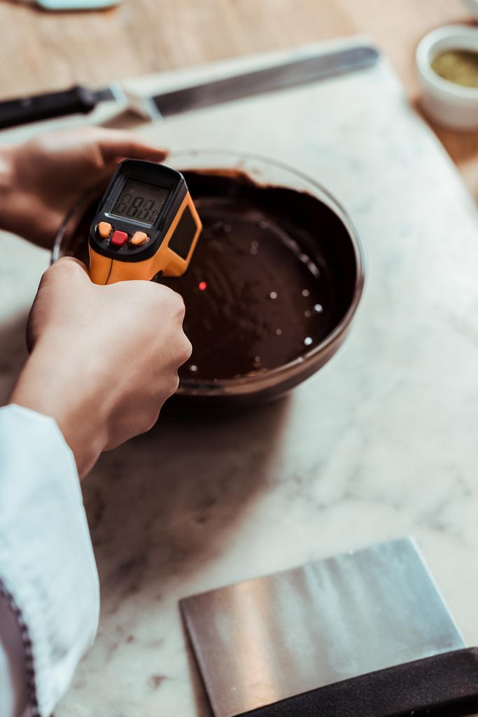 vista cortada de chocolate segurando termômetro de cozinha perto da tigela com chocolate escuro derretido
  - Foto, Imagem