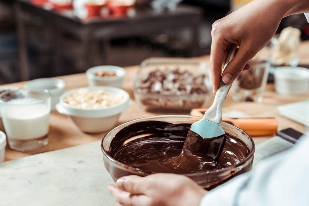 zugeschnittene Ansicht eines Chocolatiers mit Silikonspachtel beim Mischen von Schokolade in einer Schüssel  - Foto, Bild