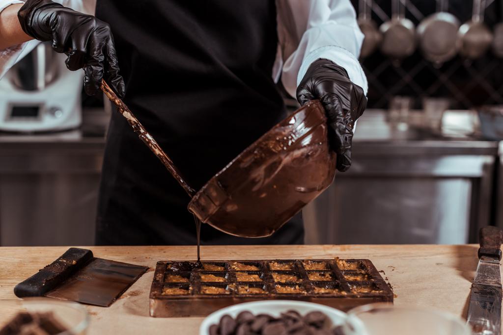 vista ritagliata della ciotola di cioccolateria mentre versava il cioccolato fuso negli stampi di cioccolato
  - Foto, immagini