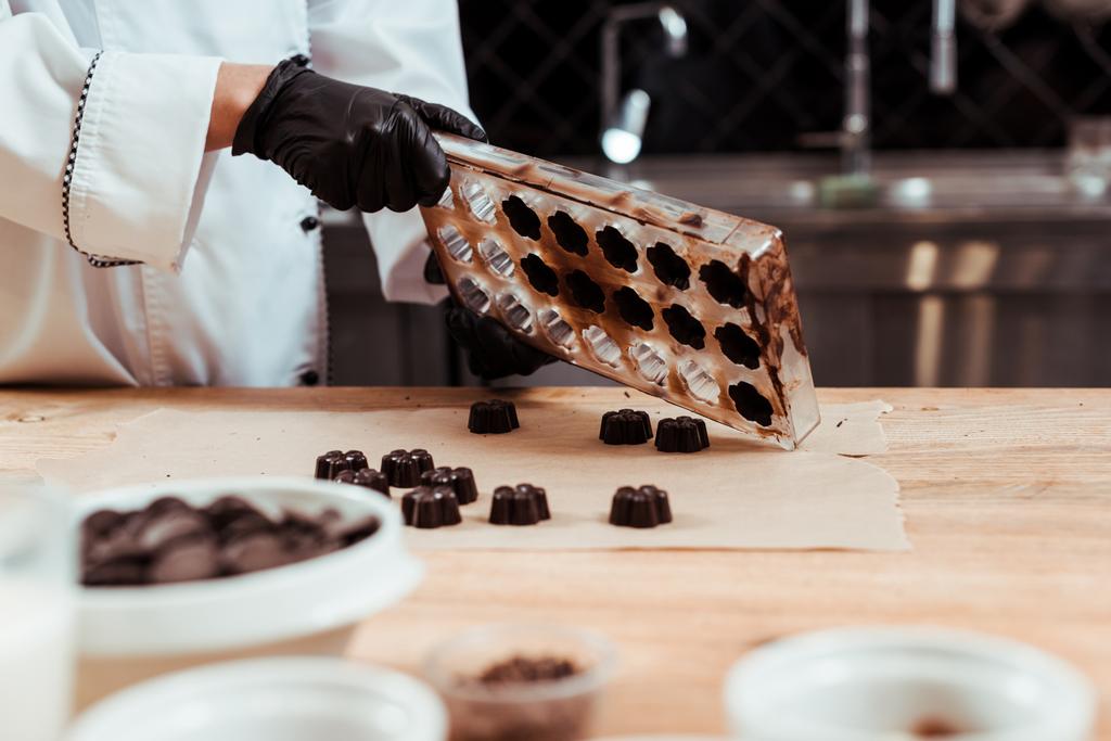 ベーキングペーパーやチョコレートキャンディーの近くにチョコレート金型を保持するショコラティエのクロップドビュー  - 写真・画像