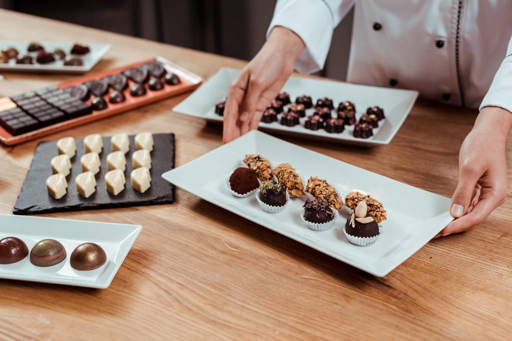 vista recortada de chocolate tocando plato con sabrosas y frescas bolas de chocolate hechas
  - Foto, imagen