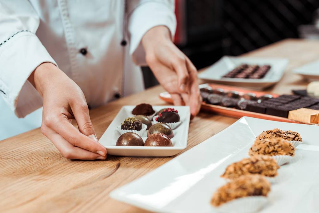 zugeschnittene Ansicht des Chocolatiers, der Teller mit Schokoladenbonbons berührt  - Foto, Bild
