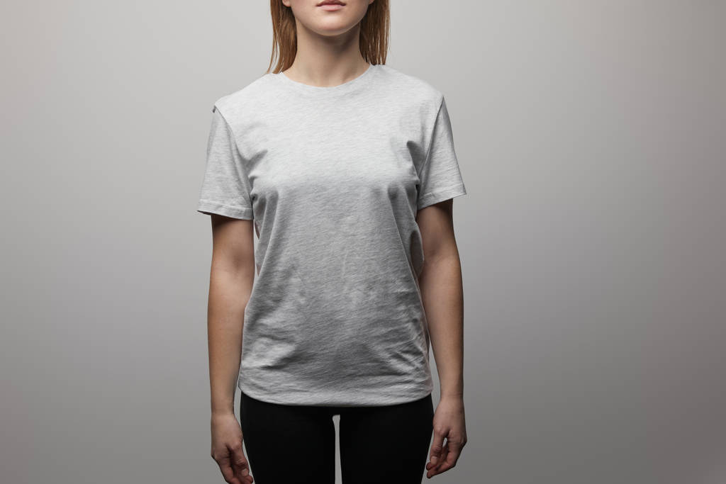 bijgesneden weergave van vrouw in blanco basic grijs t-shirt op grijze achtergrond - Foto, afbeelding