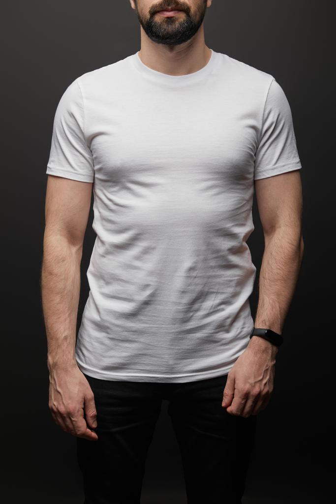 καλλιεργημένη άποψη του γενειοφόρου άνδρα σε κενό βασικό λευκό t-shirt που απομονώνονται σε μαύρο - Φωτογραφία, εικόνα