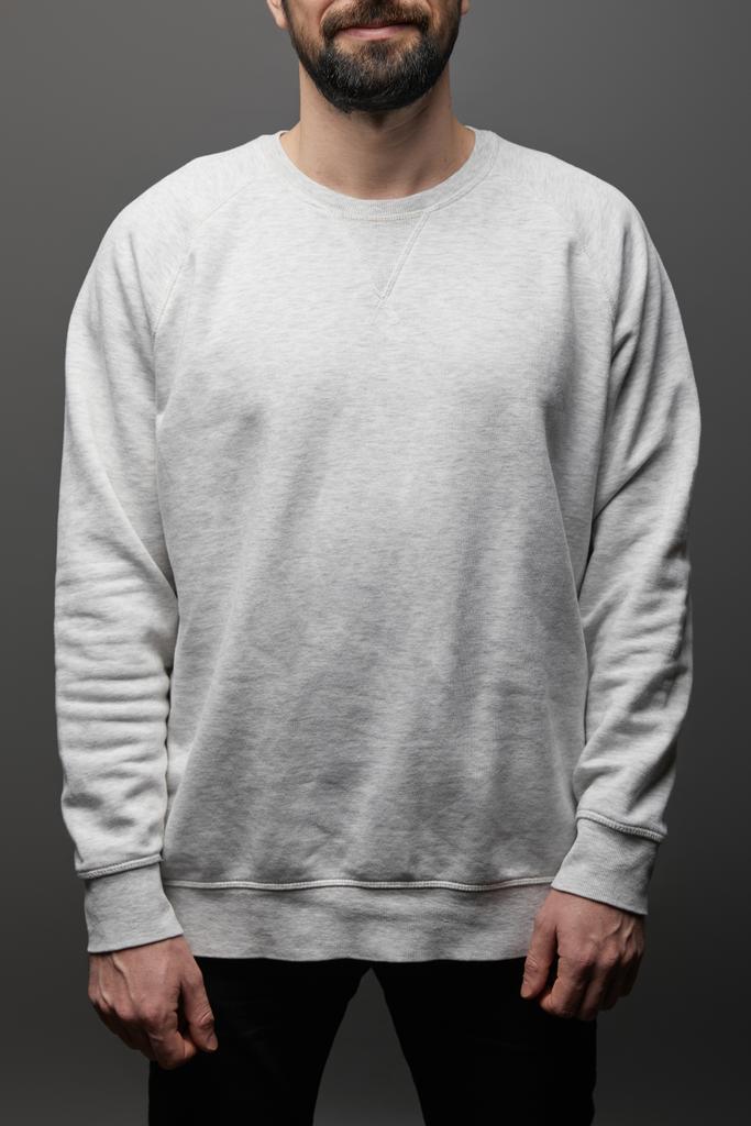 bijgesneden weergave van bebaarde man in blanco basic grijs sweatshirt op zwarte achtergrond - Foto, afbeelding