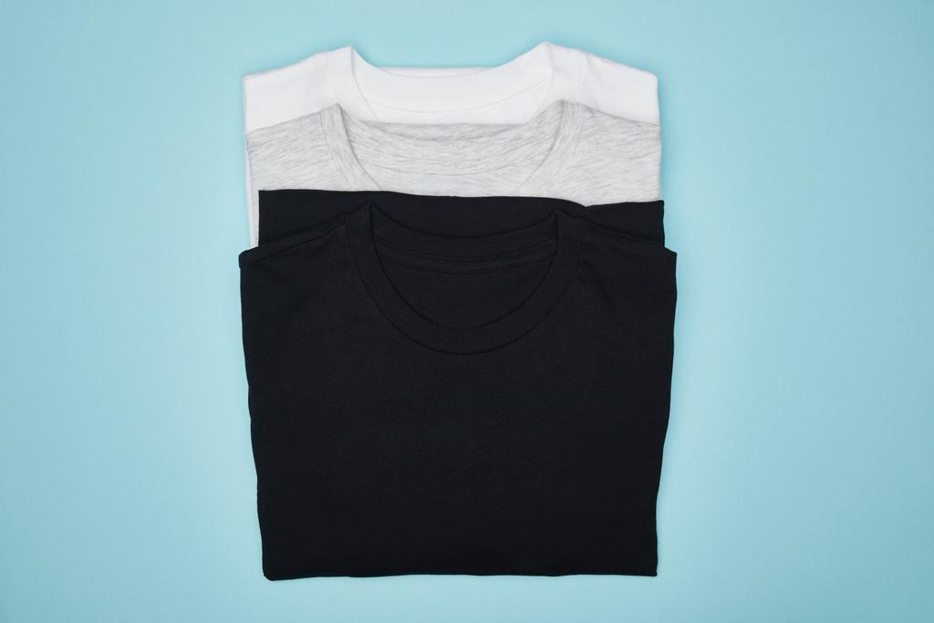 felső nézet üres alap fekete, fehér és szürke pólók elszigetelt kék - Fotó, kép