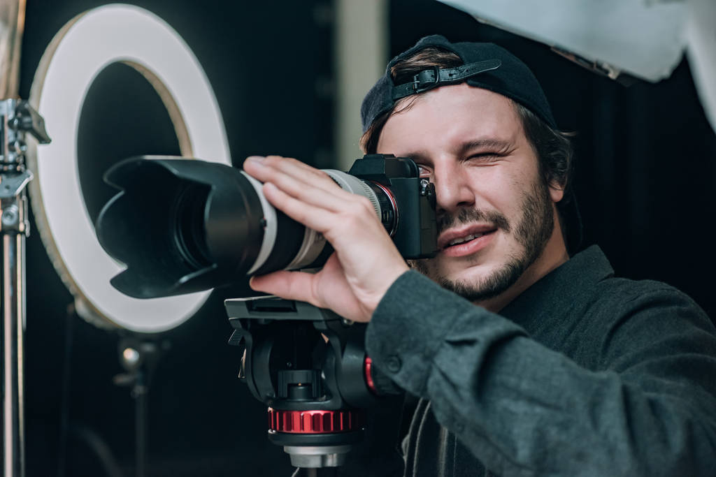 Videógrafo mirando en visor de cámara en estudio fotográfico
 - Foto, Imagen