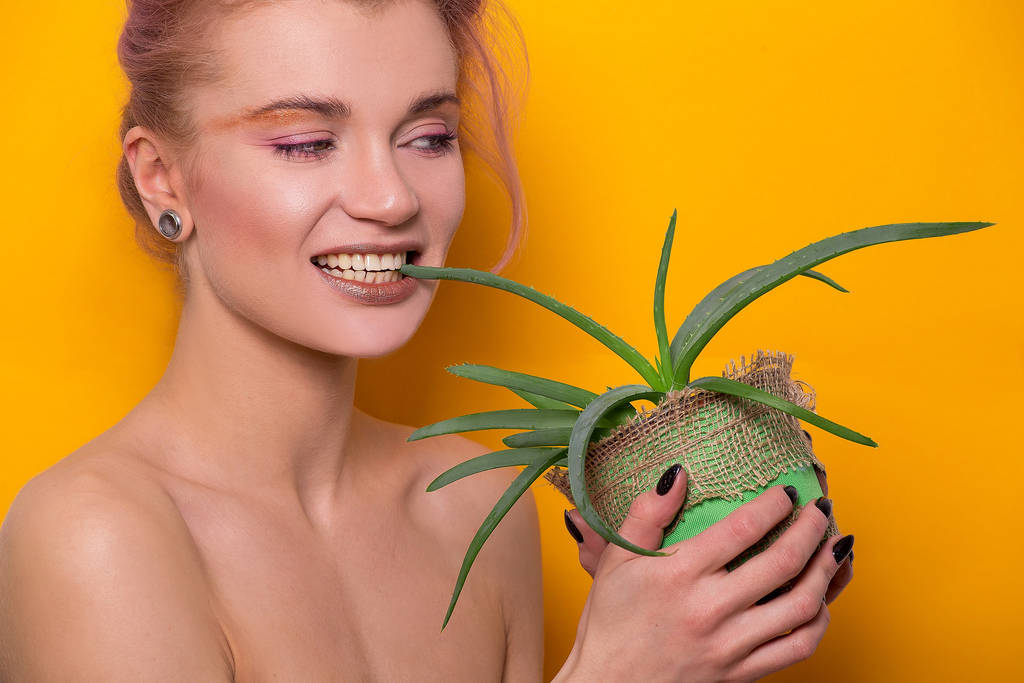 Shiny golden make-up on a beautiful young European model girl holding an aloe split in her hands isolated on an orange background in a photo studio - Photo, Image
