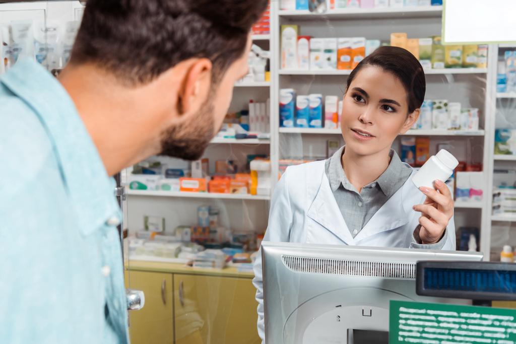 Селективный фокус аптекаря показывать банку с таблетками клиенту в аптечной кассе
 - Фото, изображение