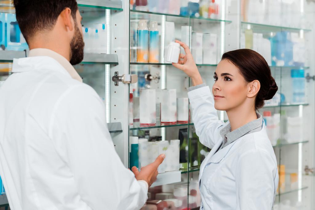 Pharmacists with jar of pills beside drugstore showcase - Photo, Image