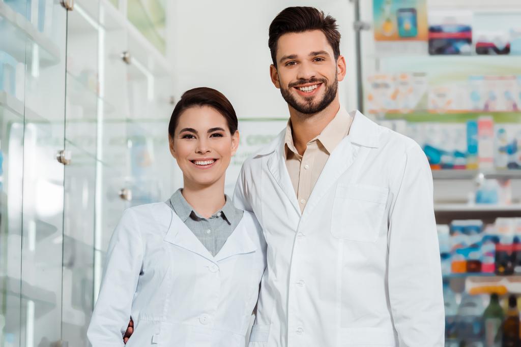 Farmacéuticos con batas blancas sonriendo a cámara en farmacia
 - Foto, Imagen