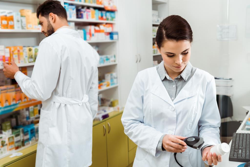 Gyógyszerész szkennelés üveg tabletták vonalkód szkenner kollégával a háttérben - Fotó, kép