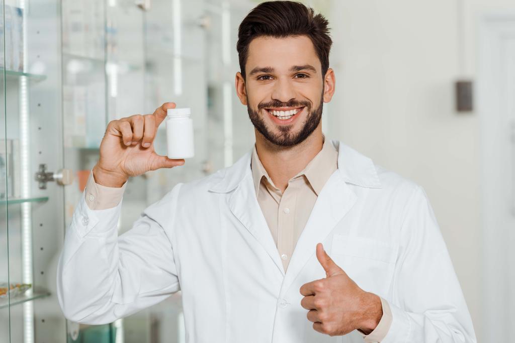 Pharmacist with jar of pills smiling at camera and showing thumb up  - Photo, Image