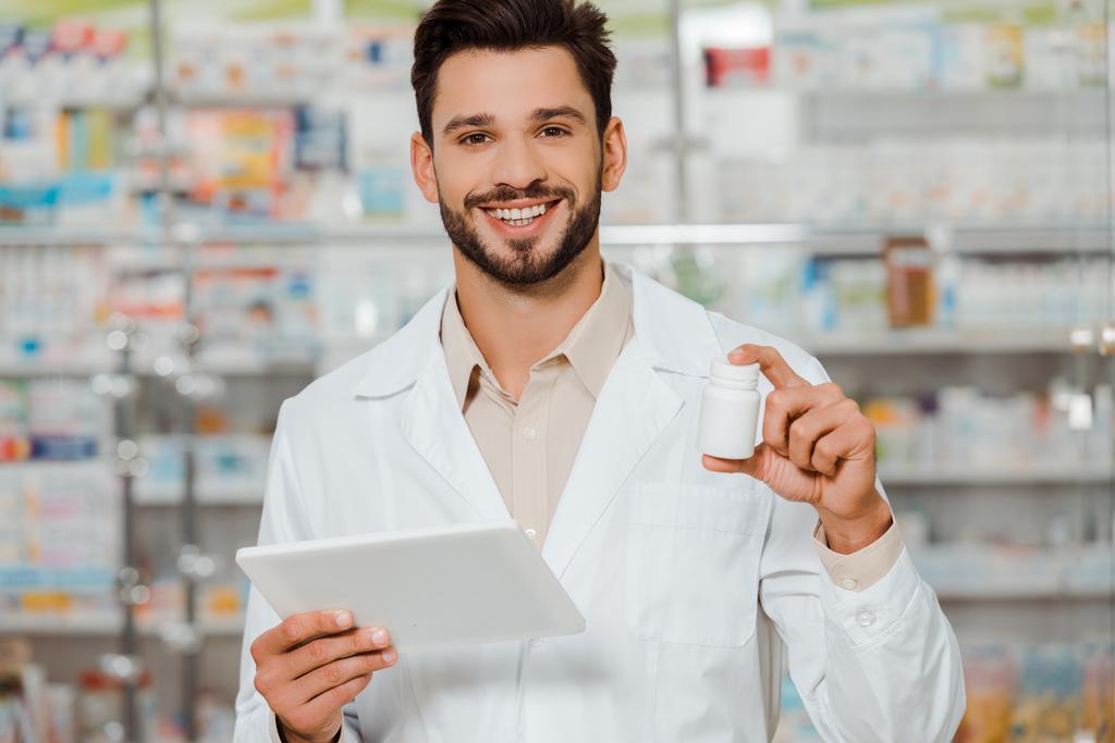 Farmacista sorridente alla macchina fotografica mentre tiene pillole e tablet digitali in farmacia
 - Foto, immagini