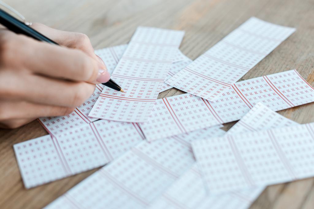 обрізаний вид жінки, що тримає ручку біля лотерейних квитків на столі
 - Фото, зображення