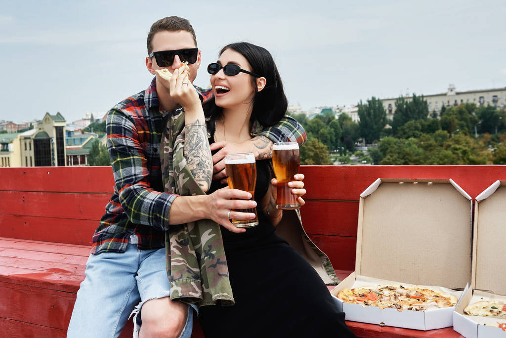 Happy smiling couple drinking beer and eating pizza at outdoor pub or bar on roof - Photo, Image