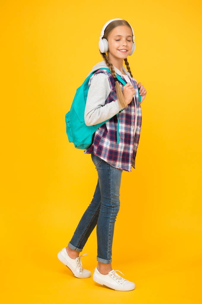 hipster κορίτσι φροντίδα σακίδιο. μαθητριούλα casual στυλ κρατήσει σχολική τσάντα. Φθινοπωρινή παιδική μόδα. παιδί ακούει μουσική ακουστικά. παιδική εκπαίδευση και ανάπτυξη. Χαρούμενη ημέρα των παιδιών. ακουστικό βιβλίο - Φωτογραφία, εικόνα