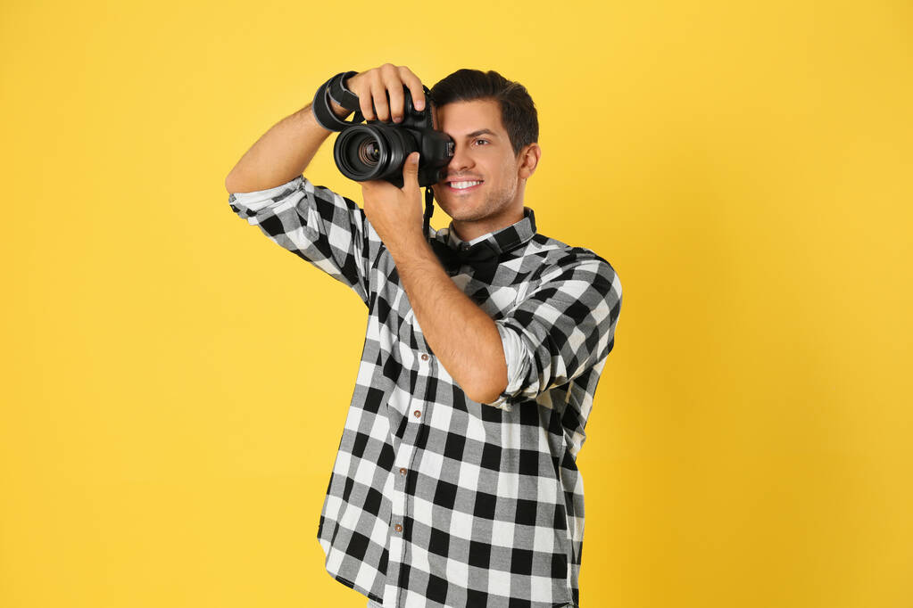 Fotógrafo profesional trabajando sobre fondo amarillo en estudio
 - Foto, Imagen
