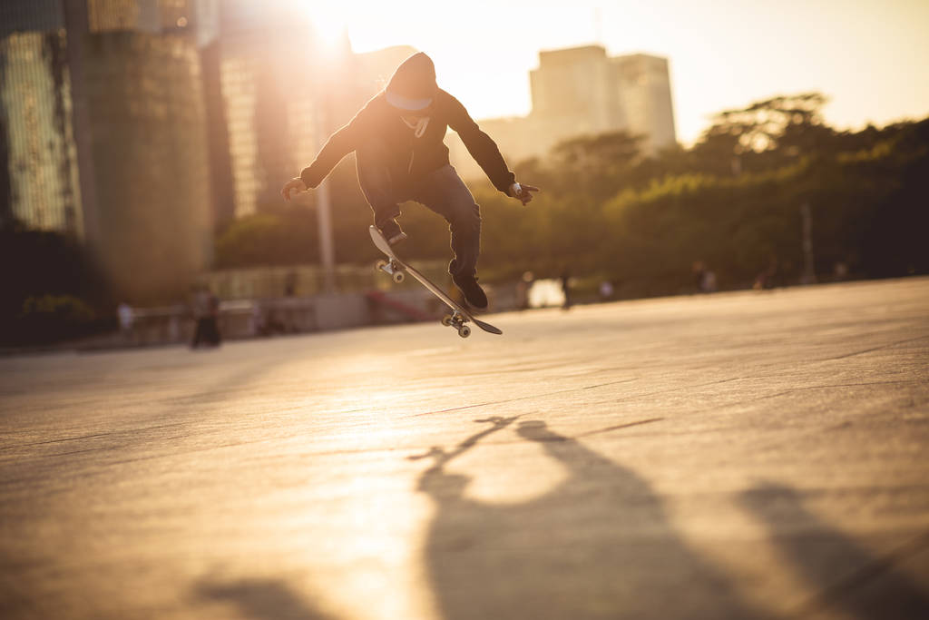 Skateboarder pulando com bordo ao pôr do sol na cidade urbana
 - Foto, Imagem