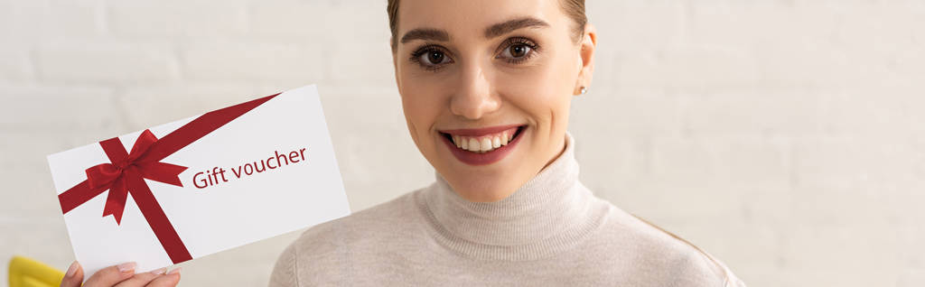 Foto panorámica de una mujer sonriente mirando a la cámara y mostrando un vale de regalo
 - Foto, Imagen