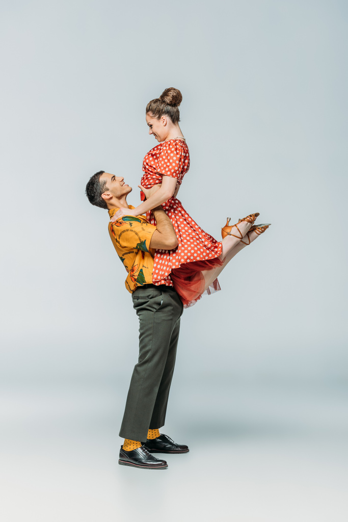 side view of handsome dancer holding partner while dancing boogie-woogie on grey background - Photo, Image