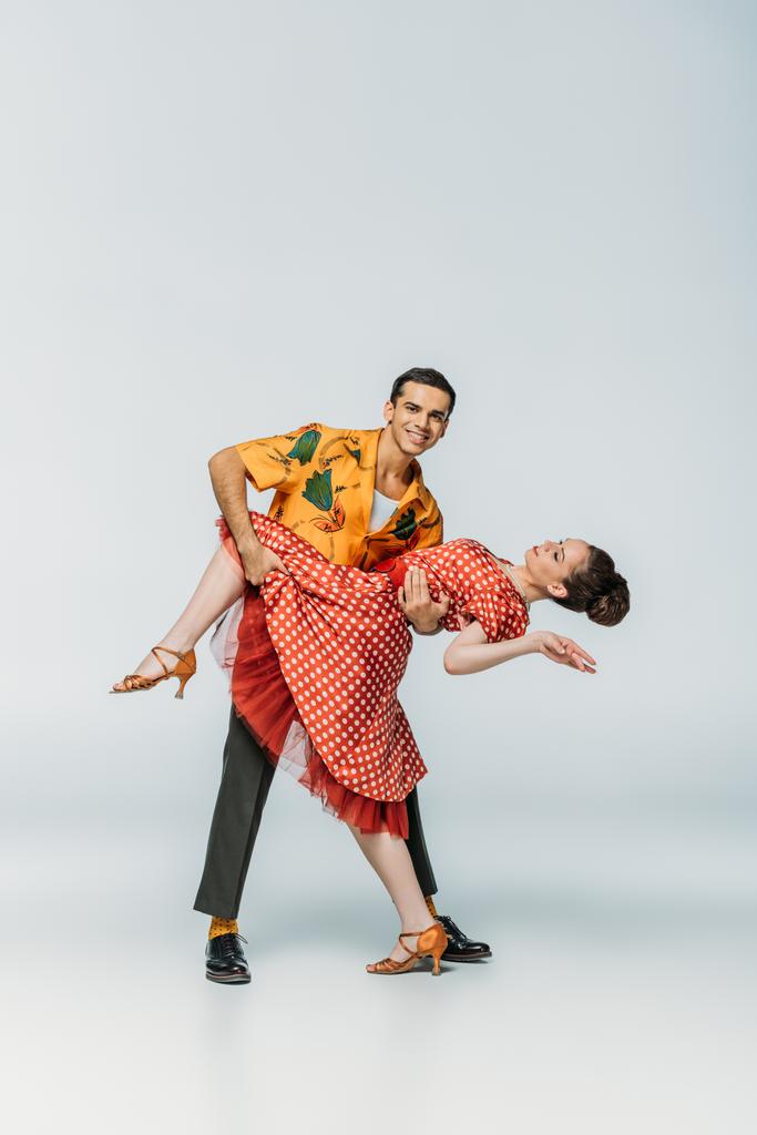 usmívající se tanečnice podporující partnera při tanci boogie-woogie na šedém pozadí - Fotografie, Obrázek