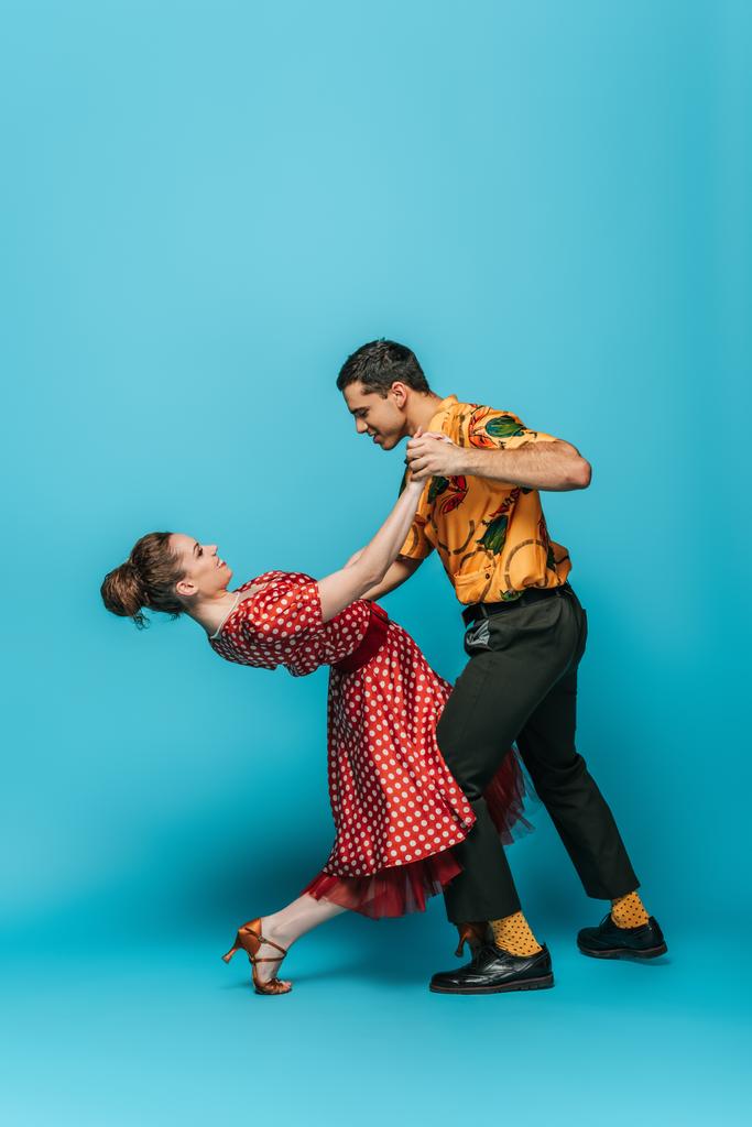side view of young dancers holding hands while dancing boogie-woogie on blue background - Photo, Image
