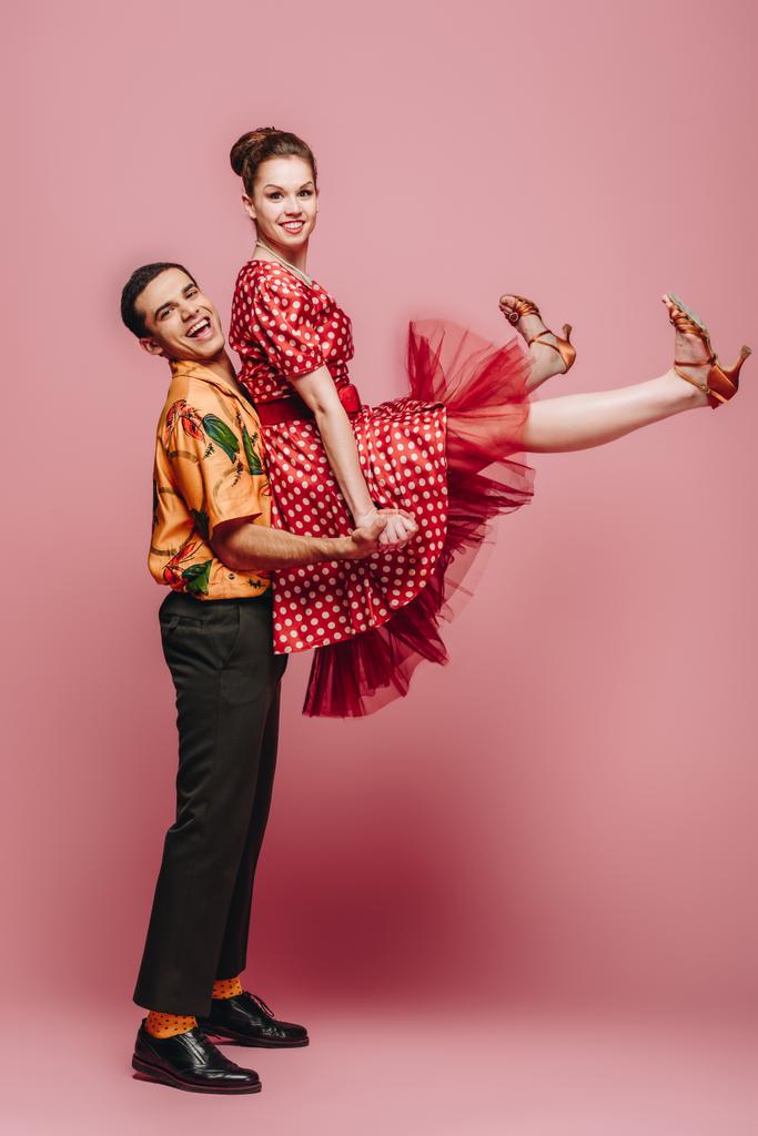 κομψό άνδρα κρατώντας γυναίκα, ενώ χορό boogie-woogie σε ροζ φόντο - Φωτογραφία, εικόνα
