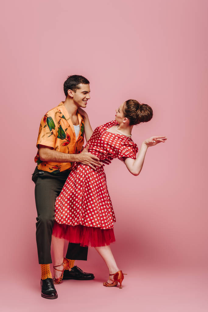 stílusos táncosok nézik egymást, miközben táncolnak boogie-woogie rózsaszín háttér - Fotó, kép