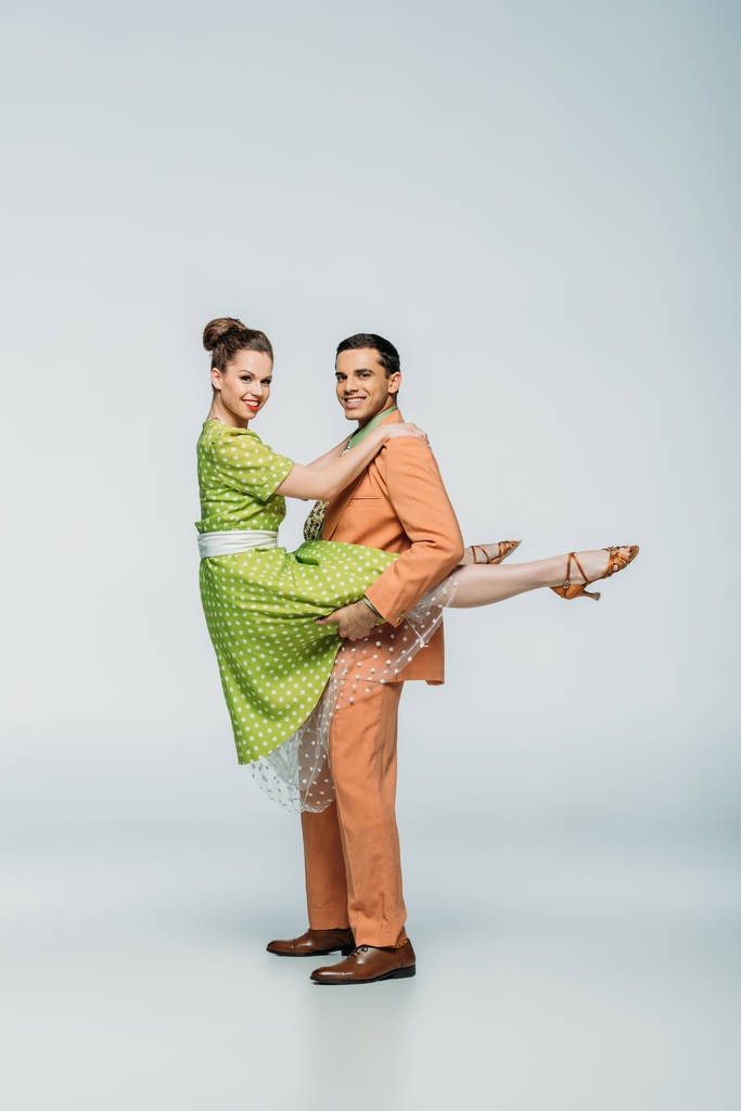 elegante bailarina sosteniendo chica mientras baila boogie-woogie sobre fondo gris
 - Foto, Imagen