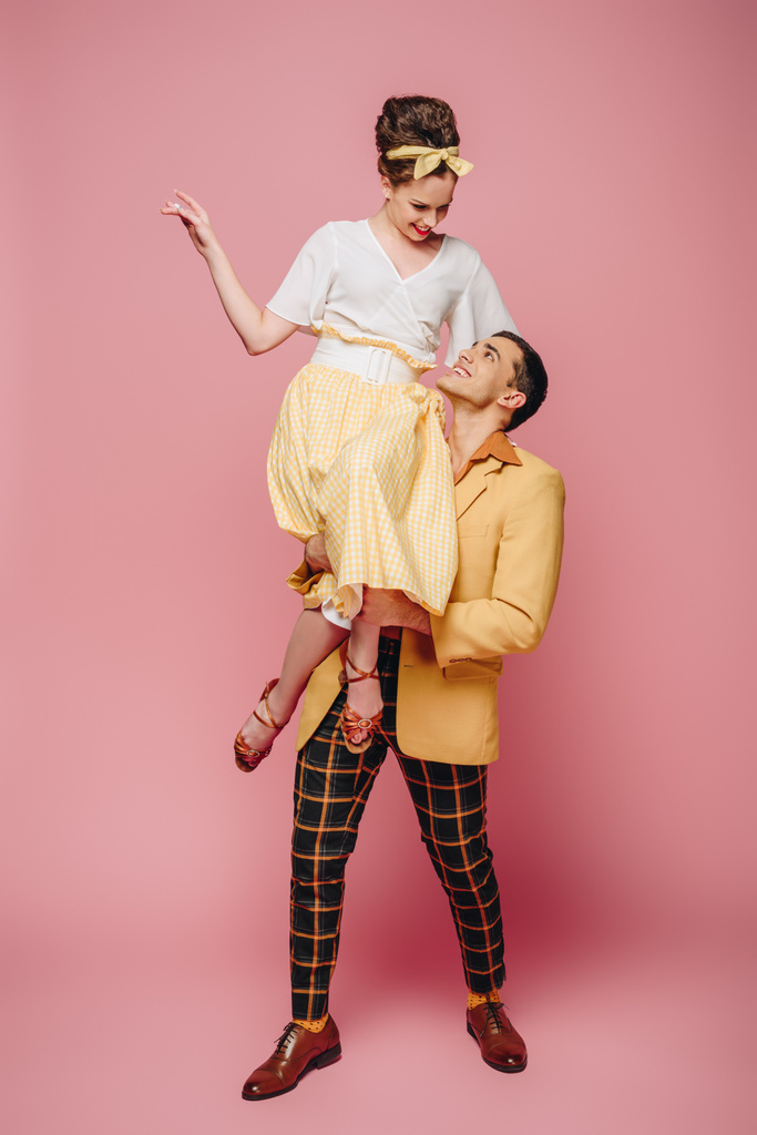 handsome man holding happy girl while dancing boogie-woogie on pink background - Photo, Image