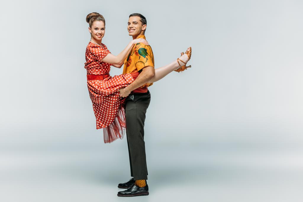 alegre hombre sosteniendo mujer mientras bailando boogie-woogie sobre fondo gris
 - Foto, imagen