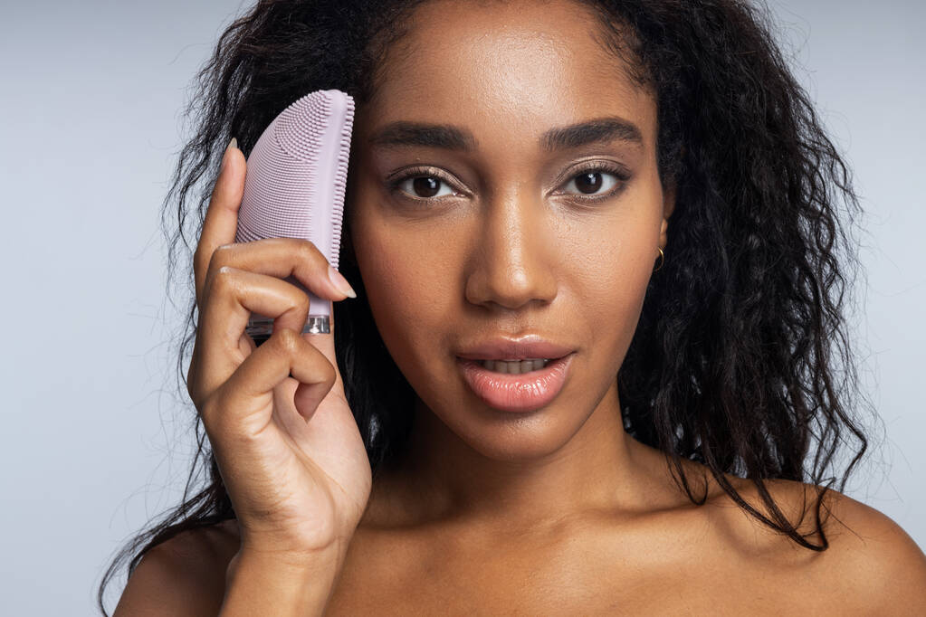 Attrayant Afro fille américaine gardant brosse en silicone pour le visage dans sa main
 - Photo, image