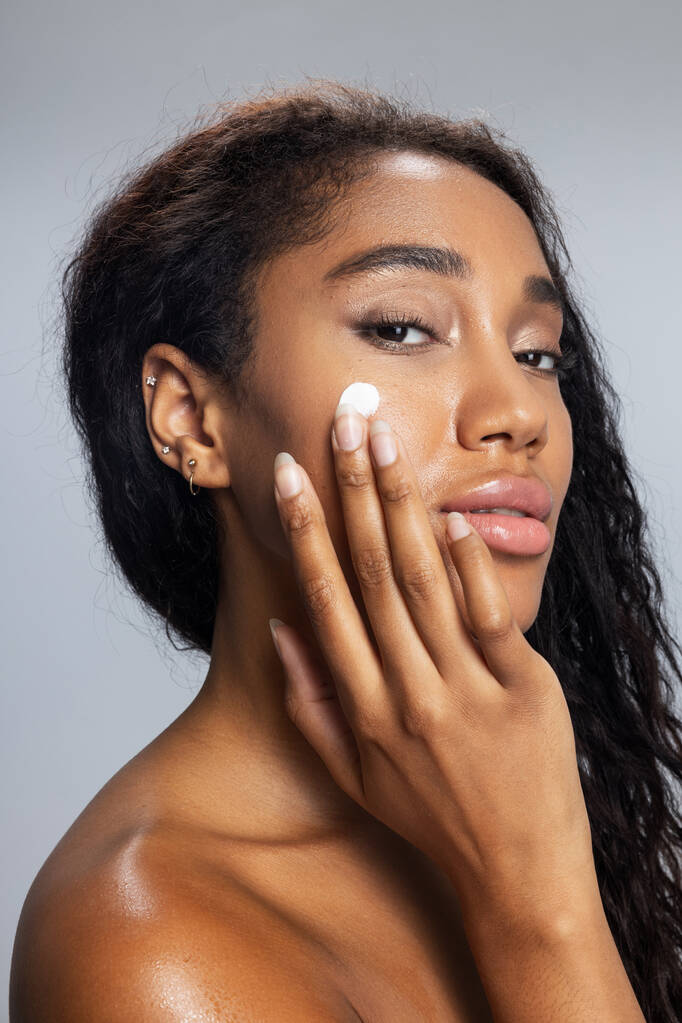 Maravillosa mujer afroamericana está aplicando crema facial
 - Foto, imagen