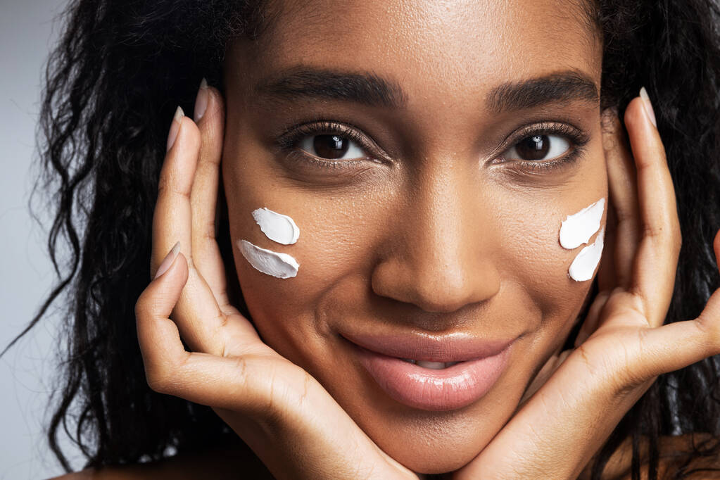 Sexy sonriente mujer afroamericana aplicando crema facial
 - Foto, Imagen