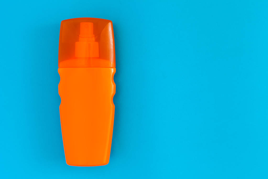 oranje fles met een spray van zonnebrand voor het looien ligt op een blauwe achtergrond bovenaanzicht, niemand. - Foto, afbeelding