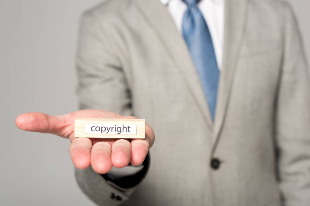 vista cortada de empresário mostrando bloco de madeira com palavra copyright isolado em cinza
 - Foto, Imagem