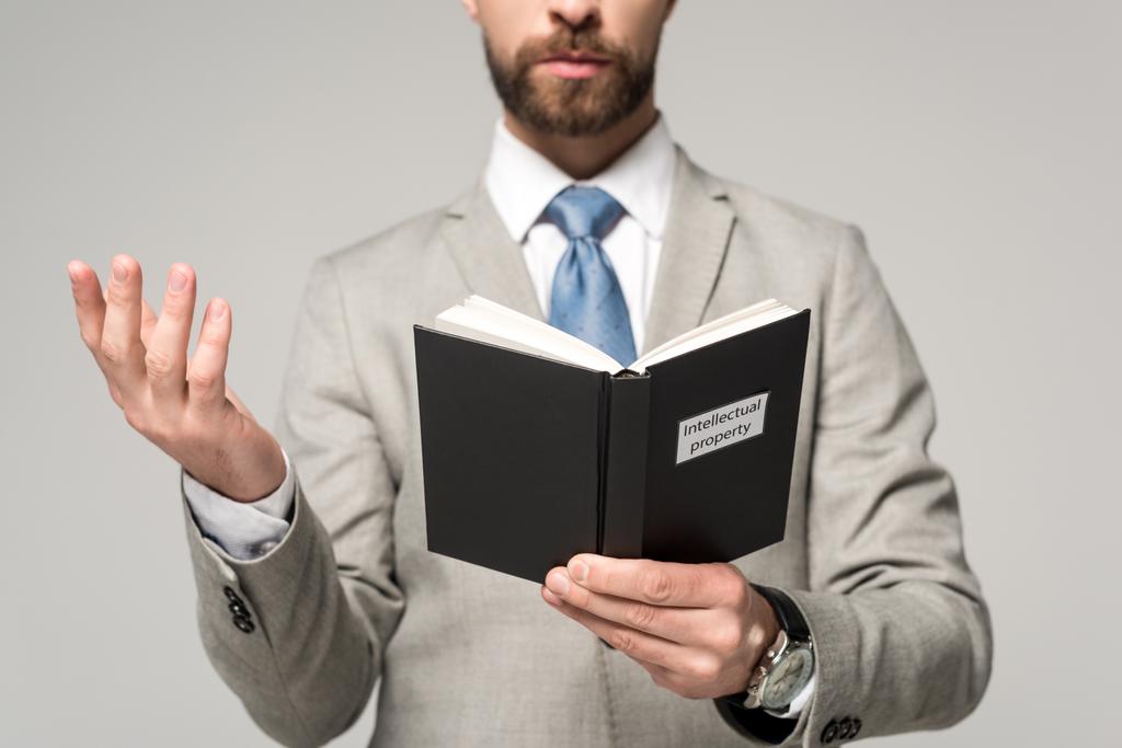 cropped view of businessman reading book with intellectual property title isolated on grey - Photo, Image
