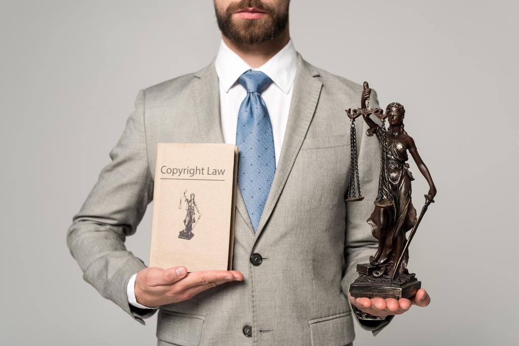 abgeschnittene Ansicht des Rechtsanwalts mit der Statue und dem Buch mit dem Titel Urheberrecht isoliert auf grau - Foto, Bild