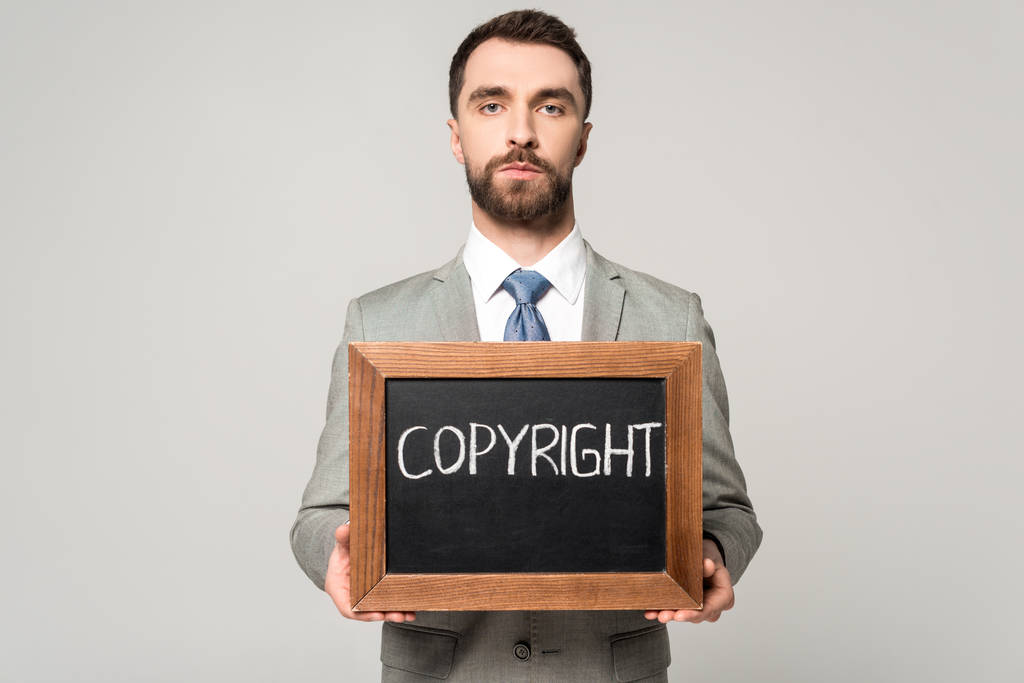 empresario seguro de sí mismo sosteniendo pizarra con letras de copyright aisladas en gris
 - Foto, imagen